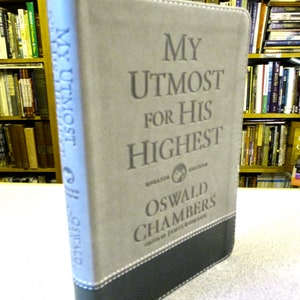 May include: A hardcover book titled "My Utmost for His Highest" by Oswald Chambers. The book has a gray cover with the title in large, embossed letters. The bottom of the book is black with white stitching.