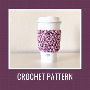 Puede incluir: Una taza de café de papel blanca con una funda de ganchillo. La funda está hecha de hilo rosa, morado y blanco. El texto "Made in USA" y "Recyclable, Reusable, & Enjoyable" está impreso en la taza. Las palabras "CROCHET PATTERN" están en la parte inferior.