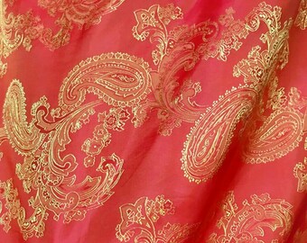 May include: Red fabric with a gold paisley pattern. The fabric is soft and flowing, and the pattern is intricate and detailed.