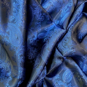 May include: Blue paisley patterned fabric with a satin finish. The fabric is folded and draped, showing the texture and pattern.
