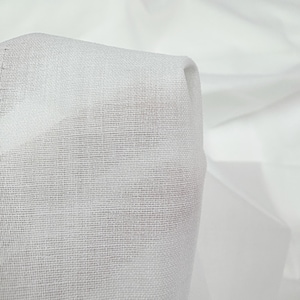 Peut inclure: Gros plan sur un tissu blanc à tissage fin et ouvert. Le tissu est plié, révélant une texture en couches et des ombres subtiles. Le matériau semble léger et semi-transparent, suggérant qu'il pourrait être utilisé pour des rideaux ou des vêtements.