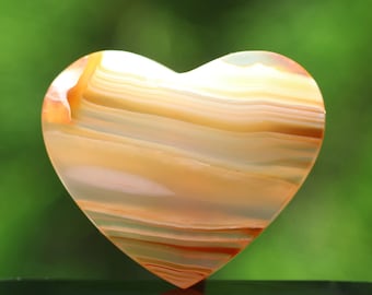 Puede incluir: Una piedra de ágata en forma de corazón con un patrón en capas y bandas en tonos de blanco, naranja y marrón.