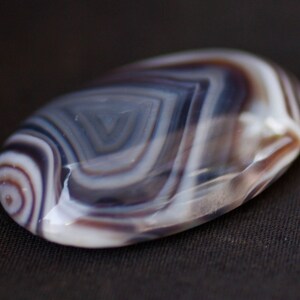 May include: A smooth, oval-shaped agate stone with intricate, swirling patterns in shades of white, gray, and brown.