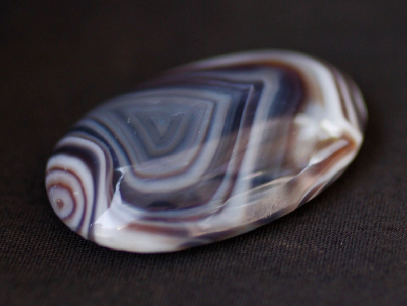 May include: A smooth, oval-shaped agate stone with intricate, swirling patterns in shades of white, gray, and brown.