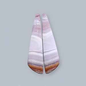 May include: A pair of teardrop-shaped earrings made from polished, layered stone. The stone is a mix of white, brown, and pink colors.