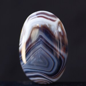 May include: A white and brown agate stone with a swirling pattern. The stone is oval shaped and has a smooth, polished surface.