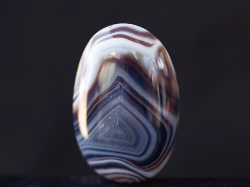 May include: A white and brown agate stone with a swirling pattern. The stone is oval shaped and has a smooth, polished surface.