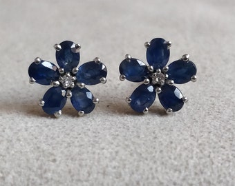 Puede incluir: Un par de pendientes de plata en forma de flor con detalles de zafiro azul y diamante.
