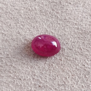 May include: A deep red oval cabochon gemstone with a smooth, polished surface.