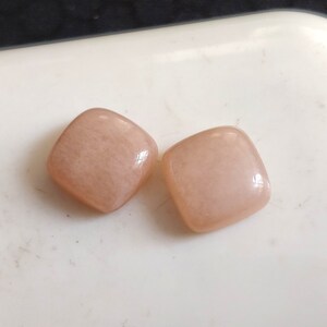 May include: Two square-shaped, light pink gemstones with a smooth, polished surface.