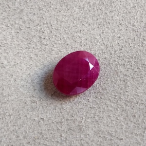 Könnte beinhalten: Ein ovaler Edelstein in tiefroter Farbe mit einem facettierten Schliff.