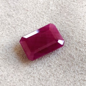 May include: A deep red gemstone with a rectangular emerald cut.
