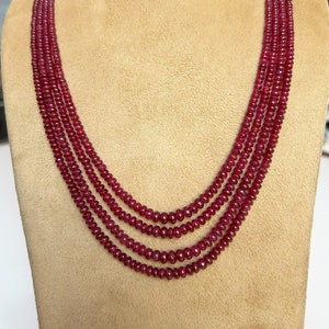 Pode incluir: Um colar de várias voltas feito de contas de rubi vermelho escuro. O colar é exibido em um busto de manequim marrom.