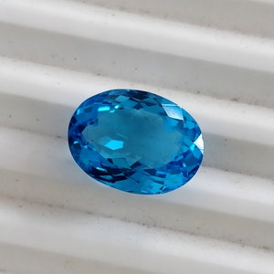 May include: A vibrant blue oval-shaped gemstone with a faceted cut. The gemstone is set against a white background.