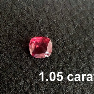 Pode incluir: Uma gema vermelha de 1,05 quilates, provavelmente um rubi, com corte almofada. A gema est&aacute; colocada sobre um fundo preto.