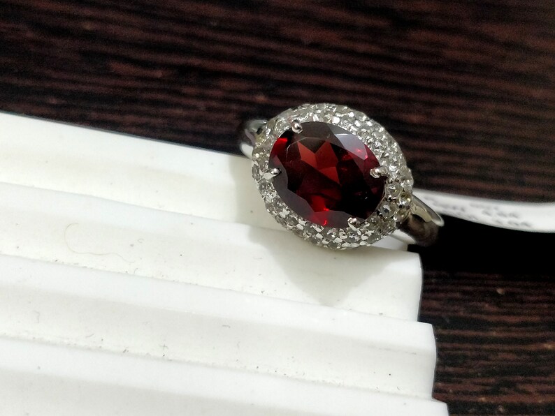 May include: A silver ring with a large oval-shaped red gemstone surrounded by smaller white gemstones.
