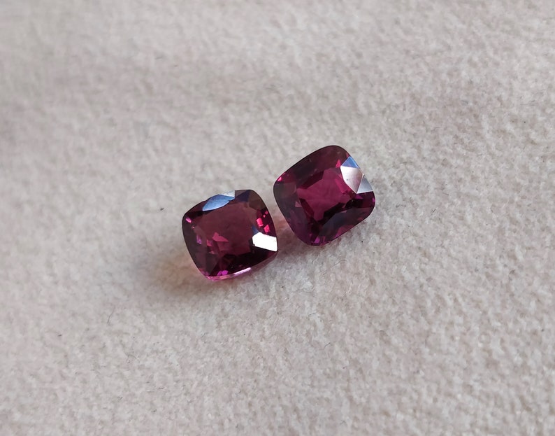 May include: Two deep red square-shaped gemstones on a white background.