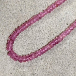 Pode incluir: Um fio de contas de pedras preciosas cor-de-rosa, enfiadas em um fio transparente. As contas s&atilde;o pequenas e redondas, e t&ecirc;m uma apar&ecirc;ncia ligeiramente facetada.