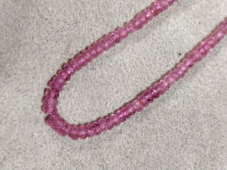 Pode incluir: Um fio de contas de pedras preciosas cor-de-rosa, enfiadas em um fio transparente. As contas s&atilde;o pequenas e redondas, e t&ecirc;m uma apar&ecirc;ncia ligeiramente facetada.