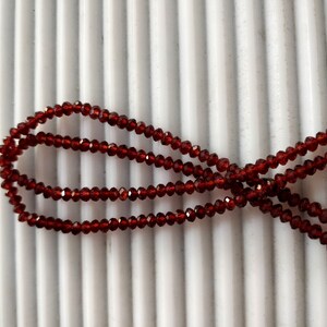 May include: A strand of dark red garnet beads, strung on a clear thread. The beads are faceted and have a shiny finish.