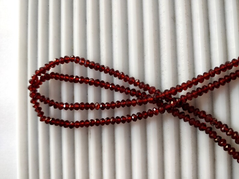 May include: A strand of dark red garnet beads, strung on a clear thread. The beads are faceted and have a shiny finish.