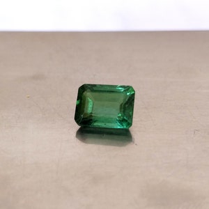 May include: A green emerald gemstone cut in an emerald shape.