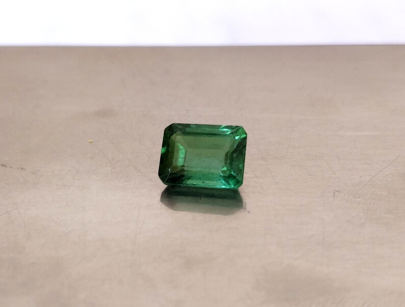 May include: A green emerald gemstone cut in an emerald shape.