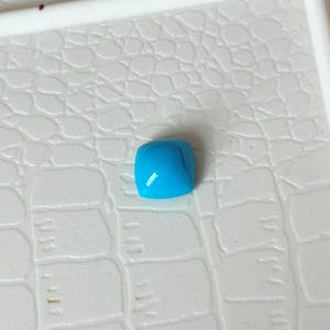 May include: A square shaped turquoise gemstone with a smooth, polished surface.
