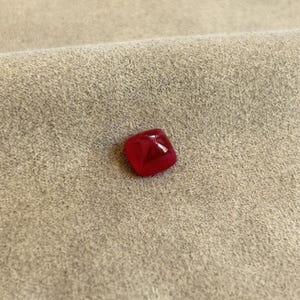 May include: A deep red square-shaped gemstone with a faceted cut.
