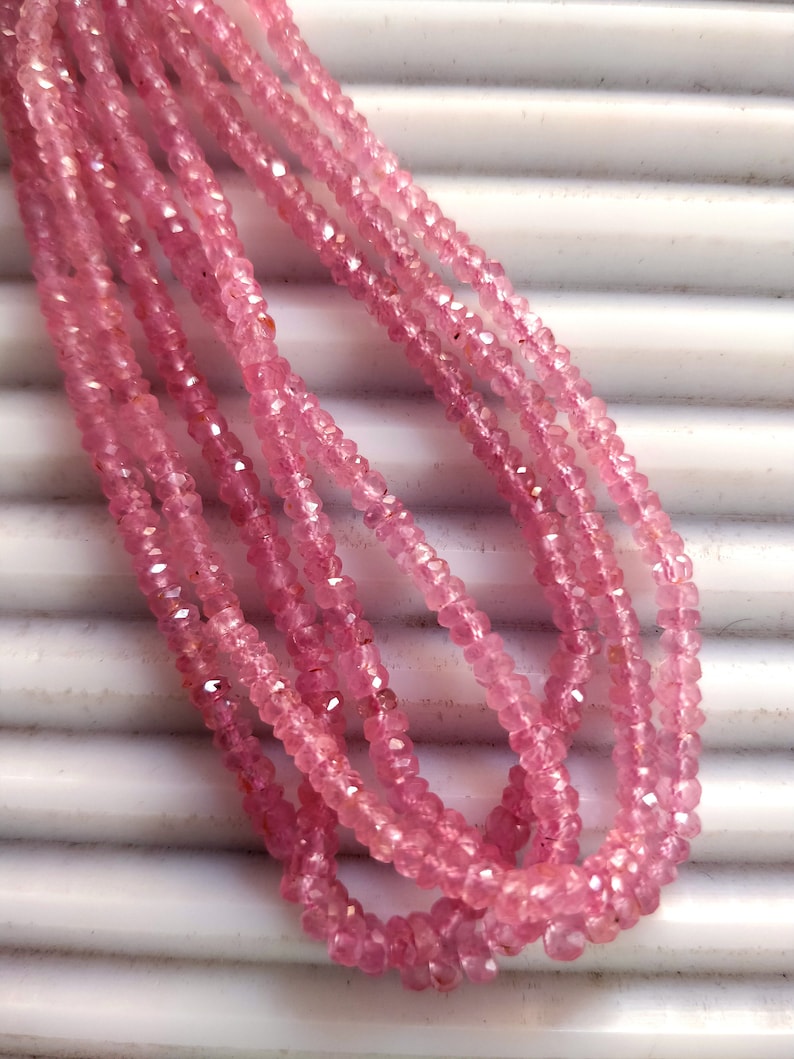 Pode incluir: Um fio de contas de pedras preciosas cor-de-rosa, provavelmente quartzo rosa, com acabamento facetado. As contas s&atilde;o enfiadas em um fio transparente e est&atilde;o dispostas em um padr&atilde;o solto e fluido.