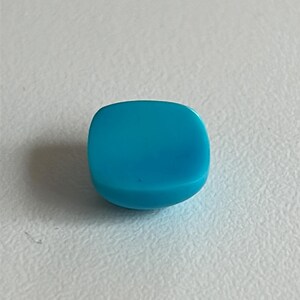 May include: A bright turquoise blue cabochon gemstone, cut in a square shape with rounded edges.