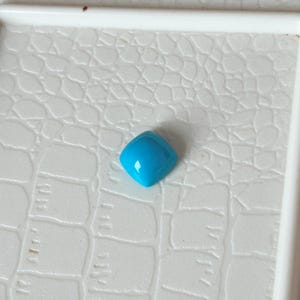 May include: A bright turquoise gemstone with a square shape and a smooth, polished surface.