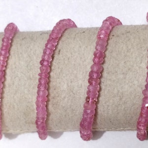 Pode incluir: Um fio de contas de pedras preciosas cor-de-rosa, provavelmente safiras cor-de-rosa, enfiadas em um cord&atilde;o branco. As contas s&atilde;o facetadas e t&ecirc;m uma forma ligeiramente irregular.