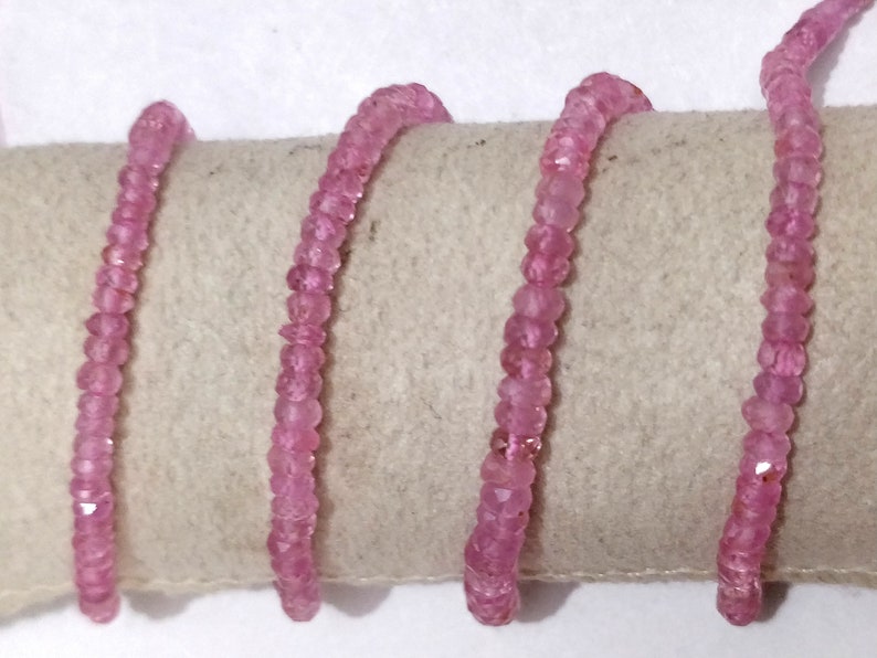 Pode incluir: Um fio de contas de pedras preciosas cor-de-rosa, provavelmente safiras cor-de-rosa, enfiadas em um cord&atilde;o branco. As contas s&atilde;o facetadas e t&ecirc;m uma forma ligeiramente irregular.