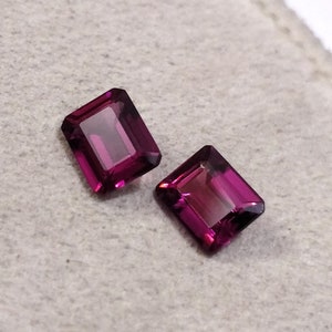 May include: Two purple gemstone rectangular cut loose stones on a white background.