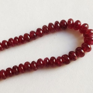 Peut inclure: Un brin de perles de rubis rouge foncé, chaque perle est ronde et légèrement allongée, créant un aspect lisse et poli.