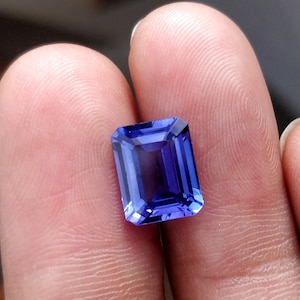 K&ouml;nnte beinhalten: Ein tiefblauer, rechteckiger Edelstein mit facettiertem Schliff. Der Edelstein wird zwischen zwei Fingern gehalten.