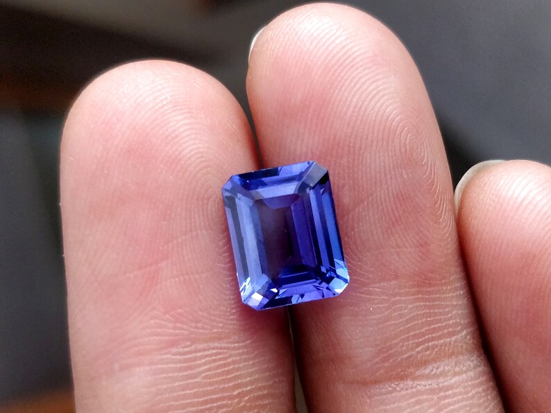 K&ouml;nnte beinhalten: Ein tiefblauer, rechteckiger Edelstein mit facettiertem Schliff. Der Edelstein wird zwischen zwei Fingern gehalten.