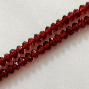 May include: A strand of dark red faceted beads. The beads are strung on a clear thread and are arranged in a double row.