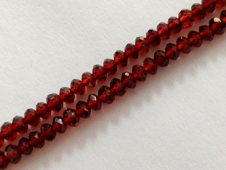 May include: A strand of dark red faceted beads. The beads are strung on a clear thread and are arranged in a double row.