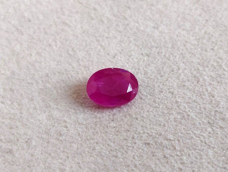 Puede incluir: Una gema ovalada de color rosa vibrante con un corte facetado.