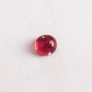 Puede incluir: Una piedra preciosa redonda de color rosa con una superficie lisa y pulida.