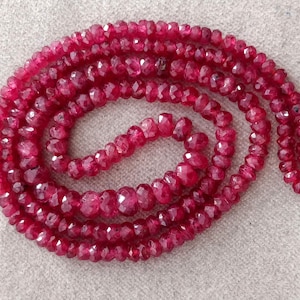 Può includere: Una collana di perle di rubino rosso, sfaccettate e infilate su un filo rosso. Le perle misurano circa 4 mm e hanno una forma sfaccettata irregolare.