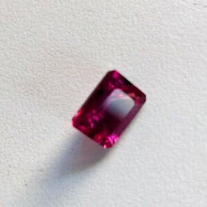 May include: A deep pink rectangular gemstone with a faceted cut.