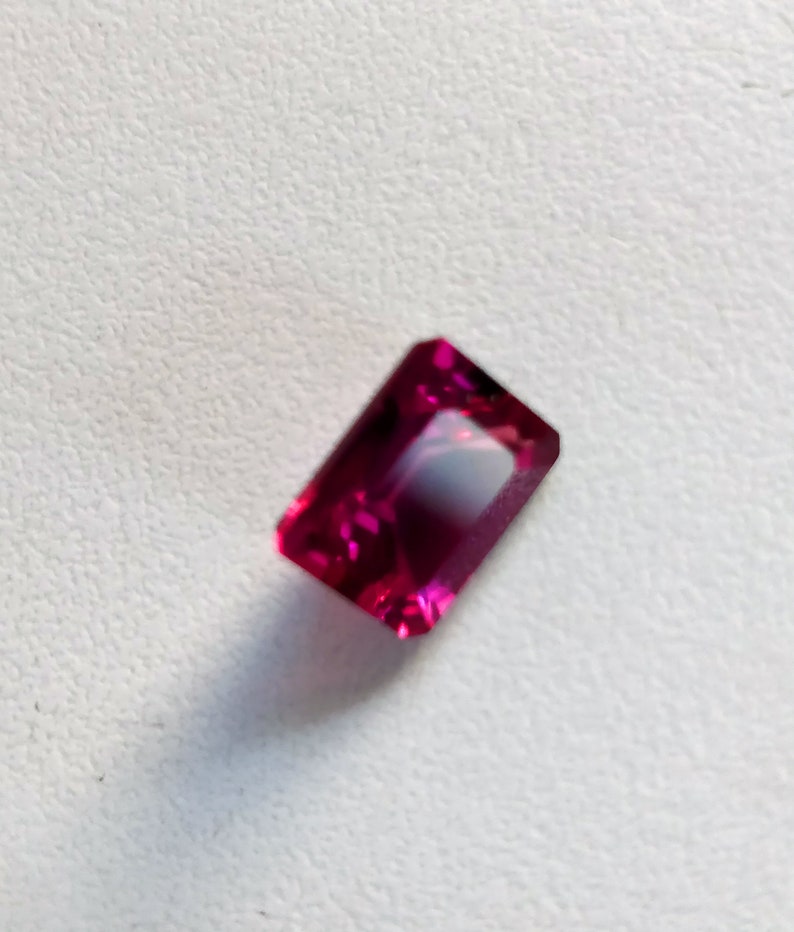 May include: A deep pink rectangular gemstone with a faceted cut.