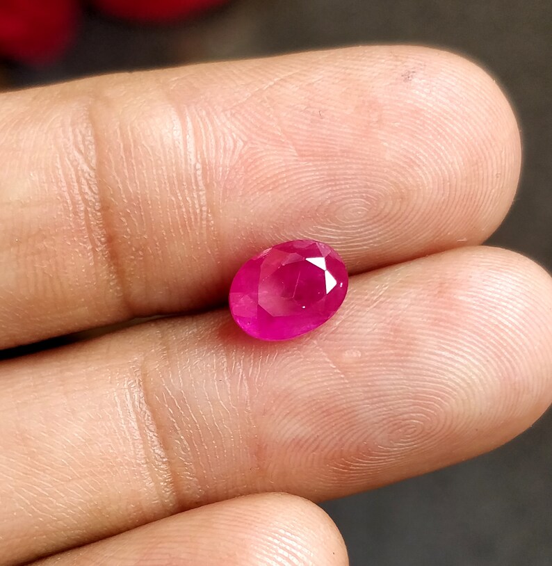 Puede incluir: Una gema ovalada de color rosa vibrante con facetas.