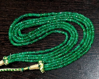 Pode incluir: Um fio de contas de pedras preciosas verde esmeralda com detalhes dourados. As contas são facetadas e têm um acabamento polido. O fio tem aproximadamente 45 cm de comprimento.