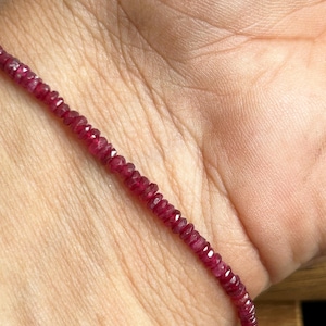 May include: A delicate strand of small, faceted ruby beads. The deep red gemstones are strung together, creating a vibrant and elegant necklace or bracelet. The beads are displayed against a skin tone background.