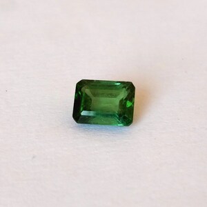 May include: A green emerald cut gemstone with a rectangular shape.