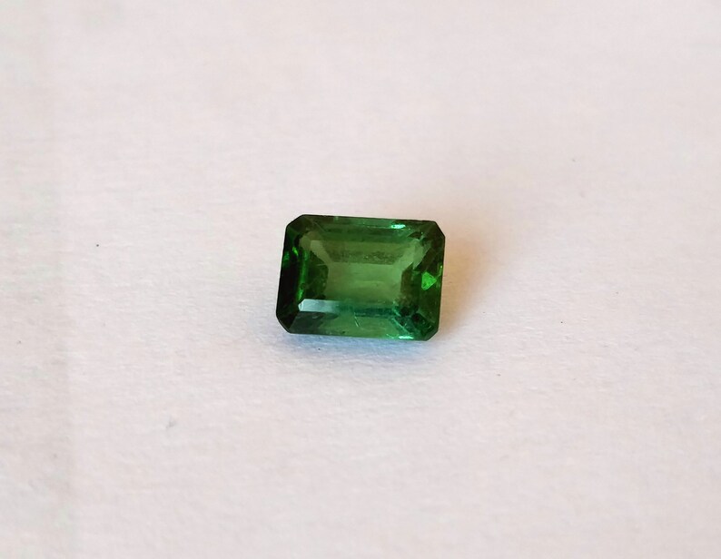May include: A green emerald cut gemstone with a rectangular shape.